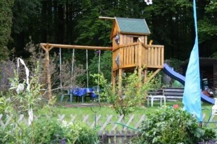 Garten mit Spielturm, Schaukel und Rutsche vor dem Waldrand